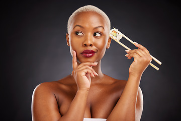 Image showing Thinking, idea and woman with sushi and chopsticks in studio for healthy eating, beauty or food. Black female model with makeup on dark background for wellness glow, diet or seafood advertising