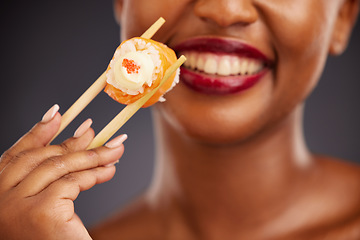 Image showing Sushi, chopsticks and mouth of a woman in studio for healthy eating, salmon or food. Black female model with makeup and smile on a dark background for wellness, diet or seafood advertising in hand