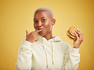 Image showing Burger, eating and portrait of woman or student on studio yellow background for restaurant promotion or deal. Hungry and happy, african person or customer experience with fast food or hamburger taste