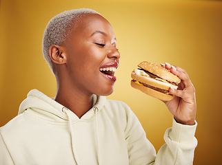 Image showing Burger, eating and young woman or student on studio, yellow background for restaurant, lunch and youth discount. Hungry and excited african person or customer experience, fast food and hamburger bite