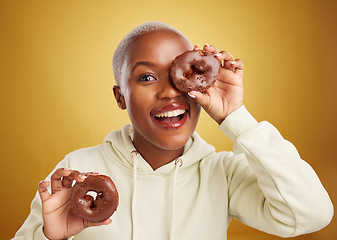 Image showing Portrait, chocolate and donut with a black woman in studio on a gold background for candy or unhealthy eating. Smile, food and baking with a happy young female person holding sweet pastry for dessert