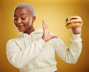 Image showing Diet, reject and fast food with woman or nutrition in yellow background is unhappy. Burger, no and girl is frustrated with choice in studio with mistake or refuse with meal for weight or health.
