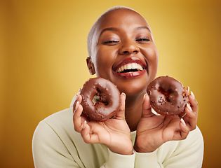 Image showing Portrait, food and donut with a black woman in studio on a gold background for candy or unhealthy eating. Smile, chocolate and baking with a happy young female person holding sweet pastry for dessert