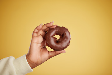 Image showing Hand, donut and chocolate dessert in studio for unhealthy eating, sugar or cake advertising. Closeup of a person with a doughnut on a yellow background for junk food, diet calories or fun emoji