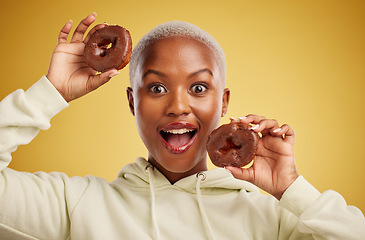 Image showing Portrait, chocolate and donut with a black woman in studio on a gold background for candy or unhealthy eating. Smile, food and baking with a happy young female person holding sweet pastry for dessert