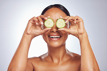 Image showing Cucumber, face and natural beauty of happy woman in studio, white background and healthy diet. Female model, skincare and fruits on eyes for sustainable cosmetics, aesthetic dermatology and nutrition