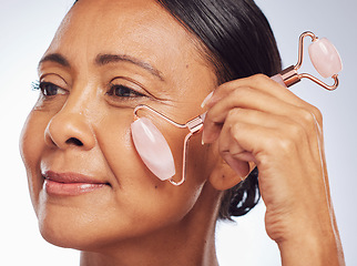 Image showing Thinking, facial or senior woman with jade roller or product for skincare massage or dermatology in studio. Beauty glow, white background or mature person smiling with natural cosmetics to relax face