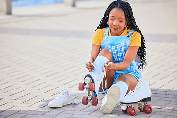 Image showing Roller skating, tie and safety with a black woman by the sea, on the promenade for training or recreation. Beach, sports and a young female teenager tying skates on the coast by the ocean or water