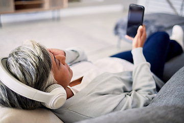 Image showing Senior woman, headphones and phone on sofa, relax and music in home living room with search, choice and listening. Elderly lady, smartphone and audio streaming app for radio, podcast and lounge couch