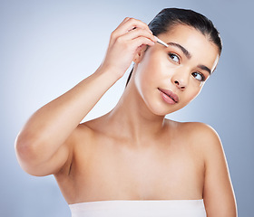 Image showing Young woman tweezing her eyebrows in a studio for grooming or hair removal face routine. Skincare, beauty and female model doing a facial epilation treatment with tweezers isolated by gray background