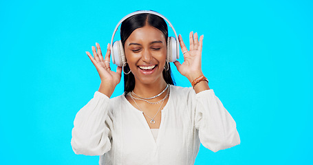 Image showing Face, music and Indian woman with headphones, streaming and happiness against blue studio background. Portrait, female and lady with headset, listening to song and dancing with success and celebrate