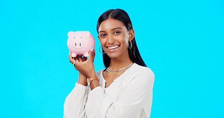 Image showing Piggy bank, happy face and Indian woman with a smile from savings, investment and finance. Isolated, blue background and portrait of a young female with happiness from cash saving and safe budget