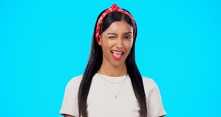 Image showing Happy woman, face and wink on blue background, laughing and flirting in studio. Portrait of indian female, model and winking with smile, fun mood and happiness of young gen z fashion, style and joy