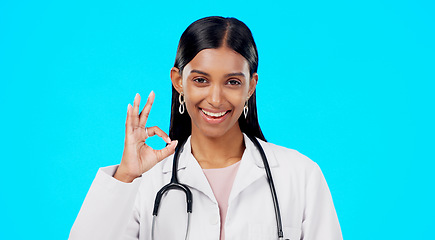 Image showing OK hand and woman doctor isolated on blue background for healthcare success and service support. Like, yes and agreement sign or emoji of Indian person or medical worker face or portrait in studio