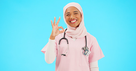 Image showing Face, nurse and Muslim woman with ok sign in studio isolated on blue background mockup. Smile, portrait and happy medical professional or Islamic person with okay emoji, hand gesture, like or success