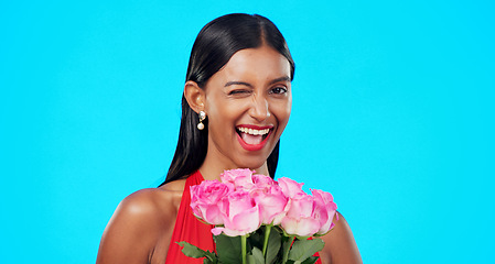 Image showing Flower bouquet, smile and beauty woman wink with nature gift, sustainable agriculture portrait or natural present. Funny flirty joke, floral studio roses and female person laugh on blue background