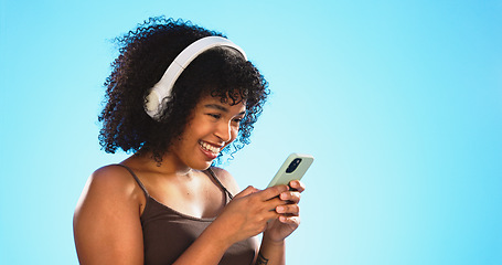 Image showing Black woman, phone and headphones isolated on blue background listening to music, social media video or funny meme. Happy gen z person laughing for audio tech, internet post and cellphone in studio