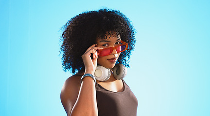 Image showing Face, sunglasses and beauty of woman in studio isolated on a blue background. Fashion portrait, smile shades and happy mixed race female model with trendy, stylish or retro, cool or gen z headphones.