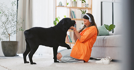 Image showing Headphones, dog licking and woman in a living room feeling puppy love from pet care in a home. House, animal and young female listening to music with happiness and bonding from labrador attention