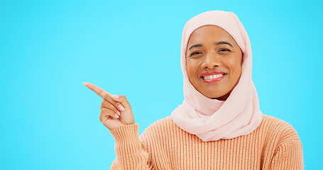 Image showing Woman, pointing finger and space for happy muslim announcement with hand for mockup. Islamic female with hijab and face with smile for sale, promotion or product placement on studio blue background