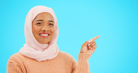 Image showing Muslim woman, happy and portrait pointing finger at space for mockup, advertising or promotion. Islam female with hand, smile and hijab for product placement announcement or sale on blue background