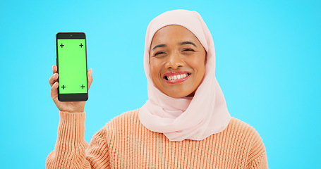 Image showing Muslim, phone or green screen and a woman on a blue background in studio holding a display with tracking markers. Islam, mobile contact and an attractive young female showing a screen for marketing