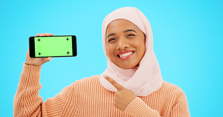 Image showing Islam, phone or green screen and a woman on a blue background in studio holding a display with tracking markers. Muslim, mobile contact and an attractive young female showing a screen for marketing