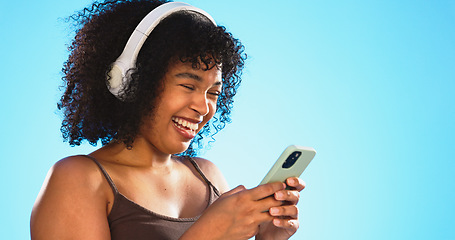 Image showing Black woman, phone and headphones isolated on blue background listening to music, social media video or funny meme. Happy gen z person laughing for audio tech, internet post and cellphone in studio