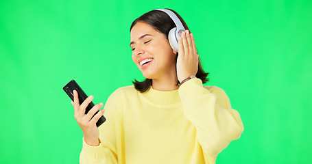 Image showing Happy woman, phone and dancing with headphones on green screen for audio track against a studio background. Female with headset listening to music on smartphone enjoying dance to sound on mockup