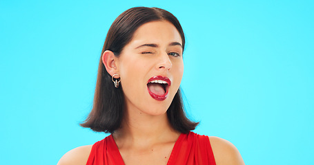 Image showing Happy, woman and winking face on blue background, studio and color backdrop. Portrait, female model and smile for wink, secret and girl in fun mood, red cosmetics and personality for flirting emoji