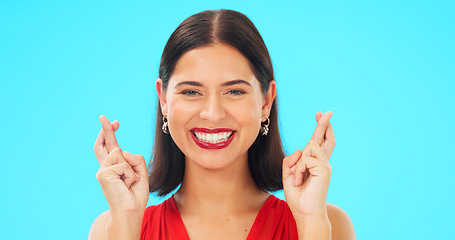 Image showing Happy, woman and face with fingers crossed on blue background, studio and wishing for good luck. Portrait of excited female model hope for winning prize, optimism and smile for emoji, hands and sign