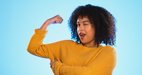 Image showing Wink, arm and bicep with a black woman joking in studio on a blue background for fun or humor. Playful, strong and muscle with an attractive young female comic flexing while winking or laughing