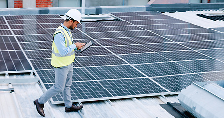 Image showing Electrician checking solar panels technology on the roof of the building his working on. Professional engineer technician wearing a safety helmet looks closely at his modern renewable energy design