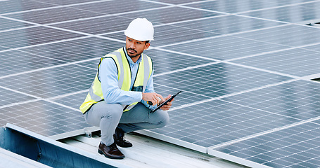 Image showing Young engineer or contractor inspecting solar panels on a roof in the city. One confident young manager or maintenance worker smiling while installing power generation equipment and holding a tablet