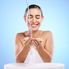 Image showing Woman, hands and water splash with smile for skincare hygiene, wash or facial treatment in sink against blue studio background. Happy female smiling in natural beauty cleanse, minerals or self care