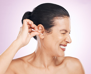 Image showing Woman, cotton bud and ear in studio for cleaning, struggle or pain for wellness by pink background. Model hand, self care or clean for hygiene, ears or natural product for healthy hearing by backdrop