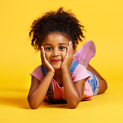 Image showing Smile, cute and portrait of a child on the floor isolated on a yellow background in a studio. Adorable, sweet and an innocent girl lying down looking happy, beautiful and relaxed on a backdrop