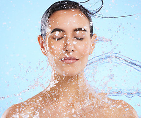 Image showing Water, splash and skincare with a woman in studio on a blue background for beauty, hygiene or hydration. Relax, wellness and cleaning with an attractive young female in the shower for self care