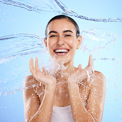 Image showing Water splash, portrait and happy woman cleaning on blue background, studio and excited for wellness skincare. Female model, smile and shower for beauty, facial hydration and aqua on color backdrop