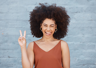 Image showing Black woman, portrait and tongue out with peace sign and afro against a gray wall background. Happy and goofy African female face smile showing peaceful hand emoji, sign and funny or silly expression