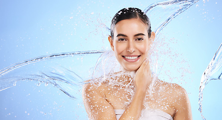 Image showing Water splash, portrait and woman shower in studio, blue background and healthy beauty of wellness skincare. Happy female model, wet and cleaning for hygiene, hydration and smile on color backdrop