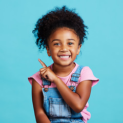 Image showing Portrait, pointing and mockup with a girl on a blue background in studio showing product placement space. Kids, marketing and advertising with an adorable female child indoor to point at branding