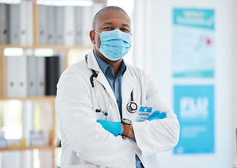 Image showing Covid, portrait and a doctor black man in a hospital office, standing arms crossed for healthcare or insurance. Medical, mask and trust with a male medicine professional at work in a wellness clinic