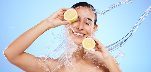 Image showing Beauty, lemon and water splash with woman in studio for natural cosmetics, nutrition and detox. Glow, fruits and hydration with female on blue background for diet, clean face and vitamin c skincare