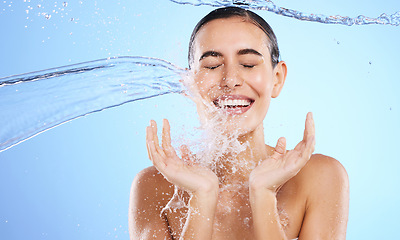 Image showing Water splash, smile and woman cleaning in studio, blue background and beauty of sustainable skincare. Happy female model, wet and shower for hygiene, facial hydration and aqua bath on color backdrop