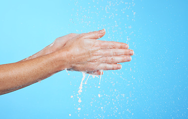 Image showing Closeup woman, water drops and washing hands on blue background, studio and backdrop for sustainability. Female model cleaning hand with liquid for showering, wellness and skincare of hygiene routine
