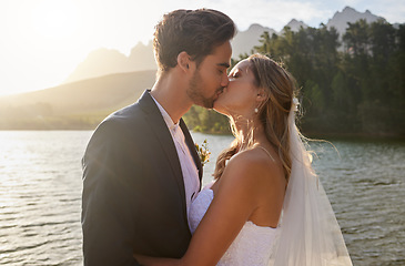Image showing Love, wedding and a newlywed couple kissing by a lake outdoor in celebration of their marriage for romance. Water, summer or kiss with a bride and groom bonding together in tradition after ceremony