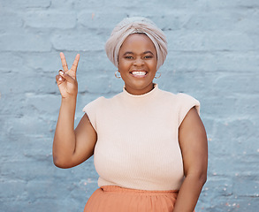 Image showing Portrait, peace and hand gesture with a business black woman on a blue brick wall with a smile. Hand, emoji and motivation with a female employee showing a v sign while feeling positive or confident