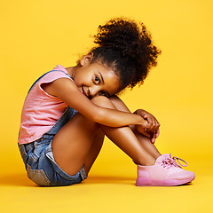 Image showing Portrait, shy and girl child on studio floor for children fashion, playful and sweet against yellow background. Face, little and smile by kid with self love, pose and relax while sitting isolated