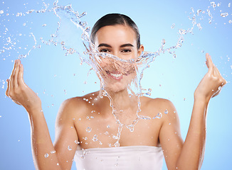 Image showing Water splash, portrait or happy woman and face wash for skincare or hygiene on blue background in studio. Smile, wet or model and clean hands in wellness washing, beauty grooming or facial treatment